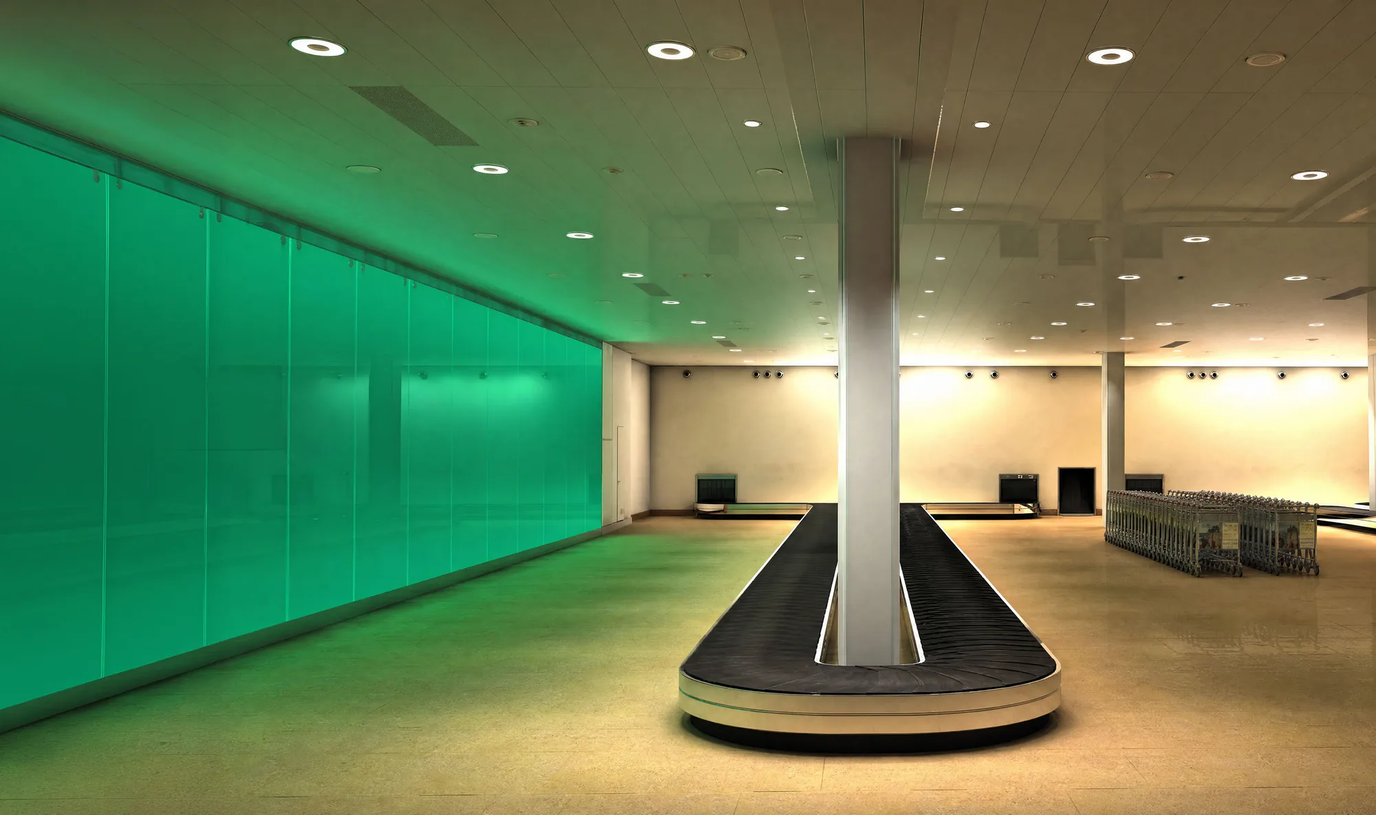 A public interior — an empty airport arrivals hall with a glowing green glass wall, warm ceiling light against 