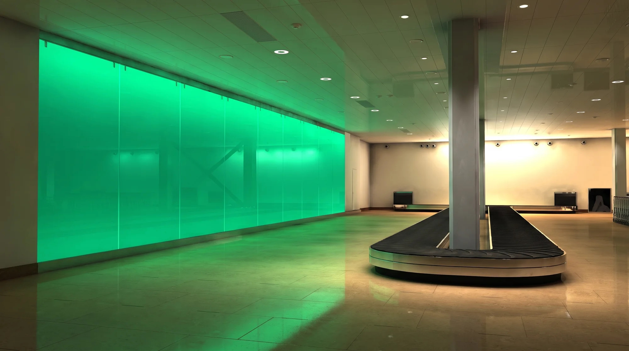 Wide view of the arrivals hall from the side, the green glass wall running the full length of the room
