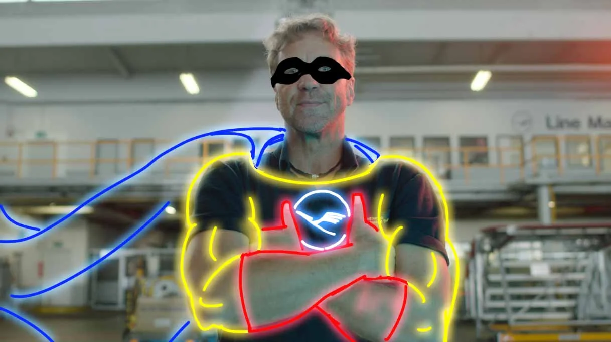A doodle paintover on a live-action still — neon cape, mask and muscles drawn over a Lufthansa Technik mechani