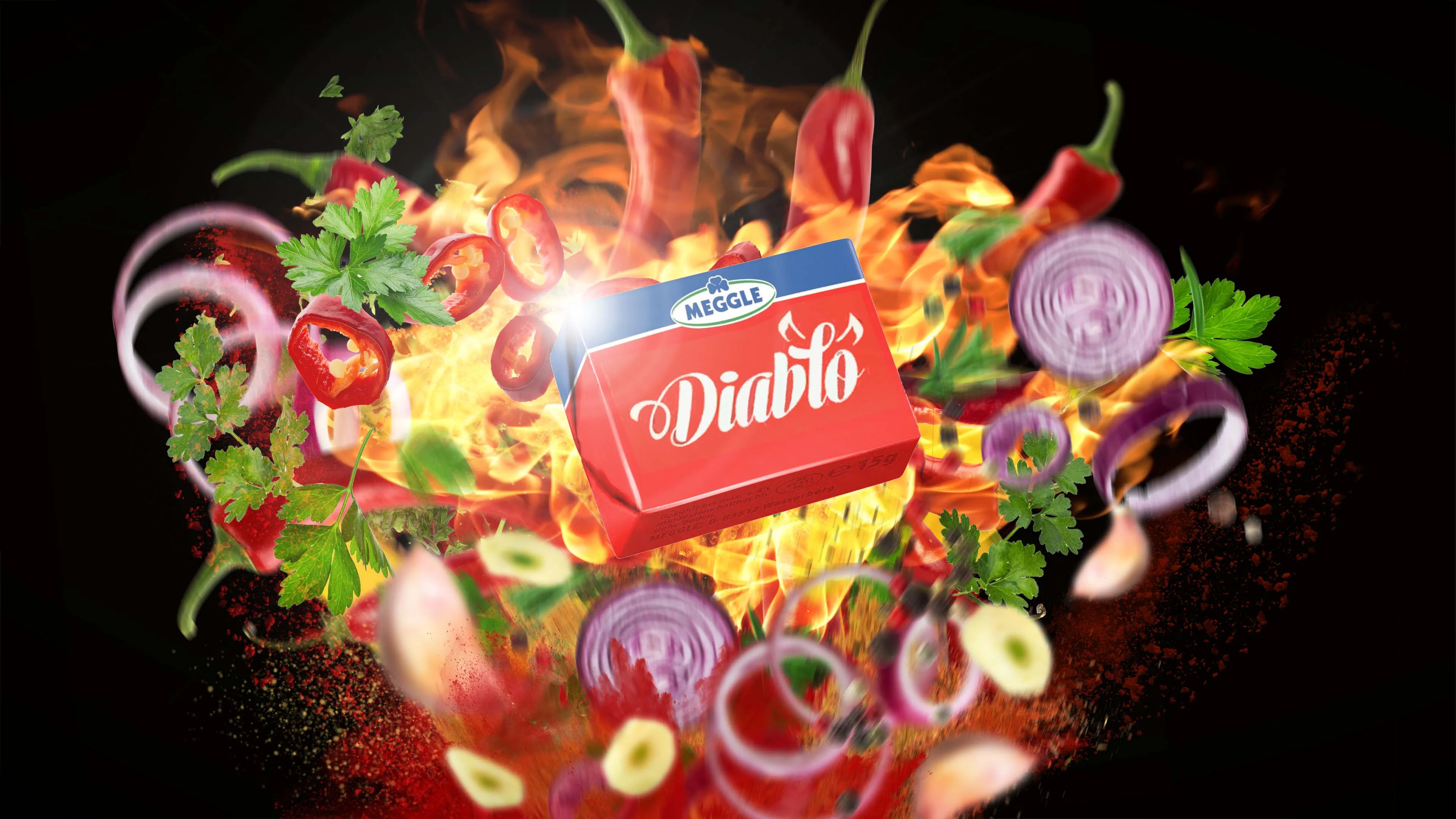 Meggle Diablo chili butter pack bursting from flames, chili peppers, parsley, red onion rings and spice, on a black backdrop