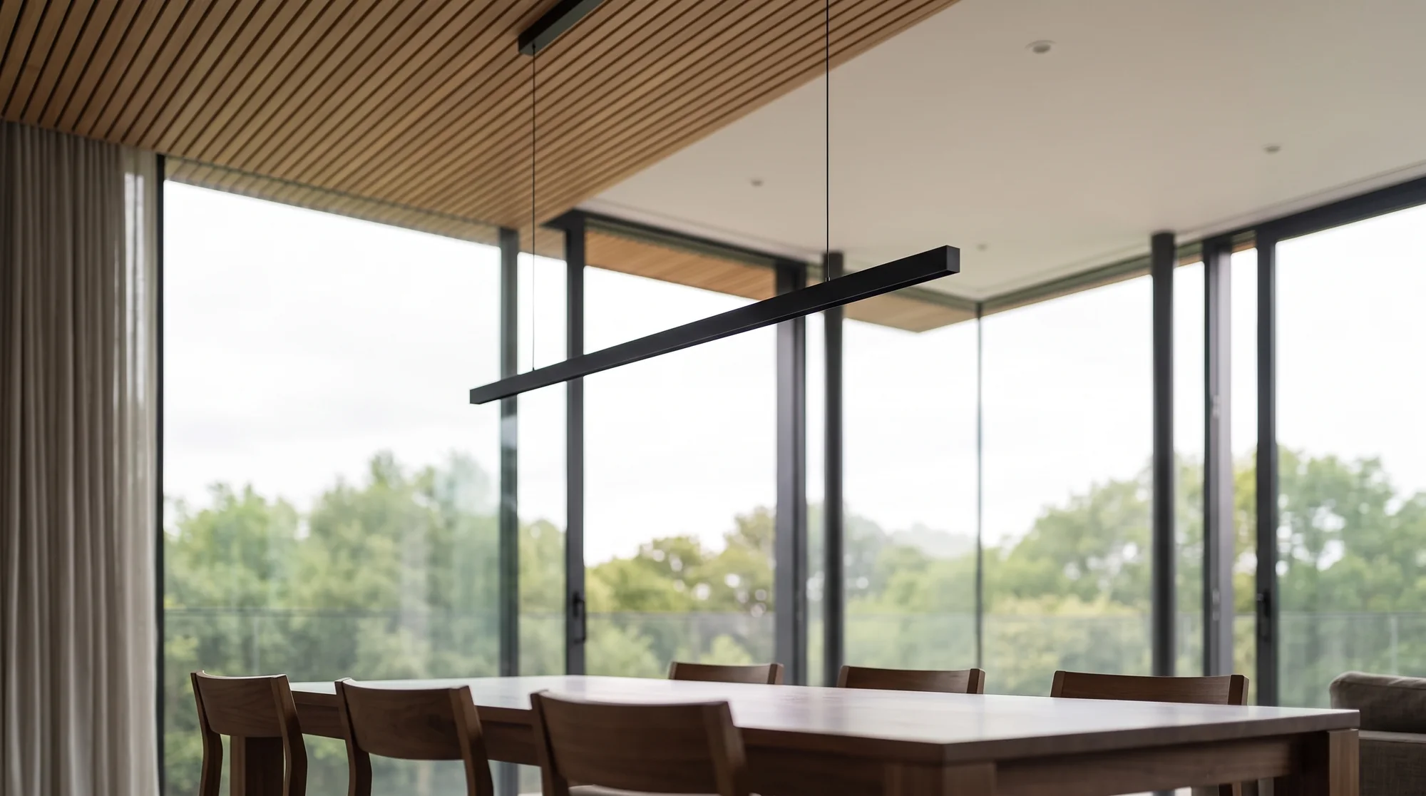 Dining area under the slatted oak ceiling with a black linear pendant, chairs and table in walnut
