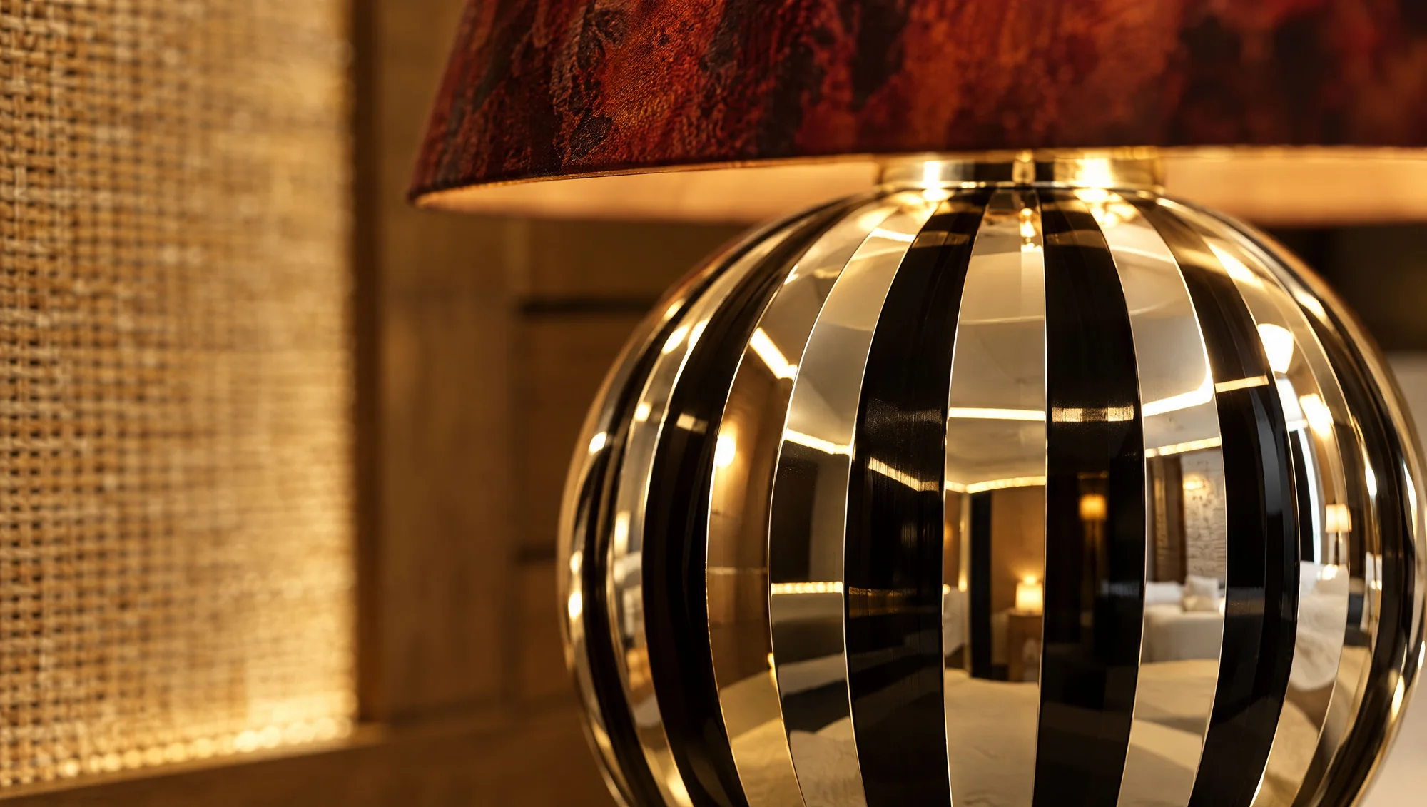 Close-up of the bedside lamp — striped chrome sphere reflecting the cabin, mottled red shade, woven panel behind
