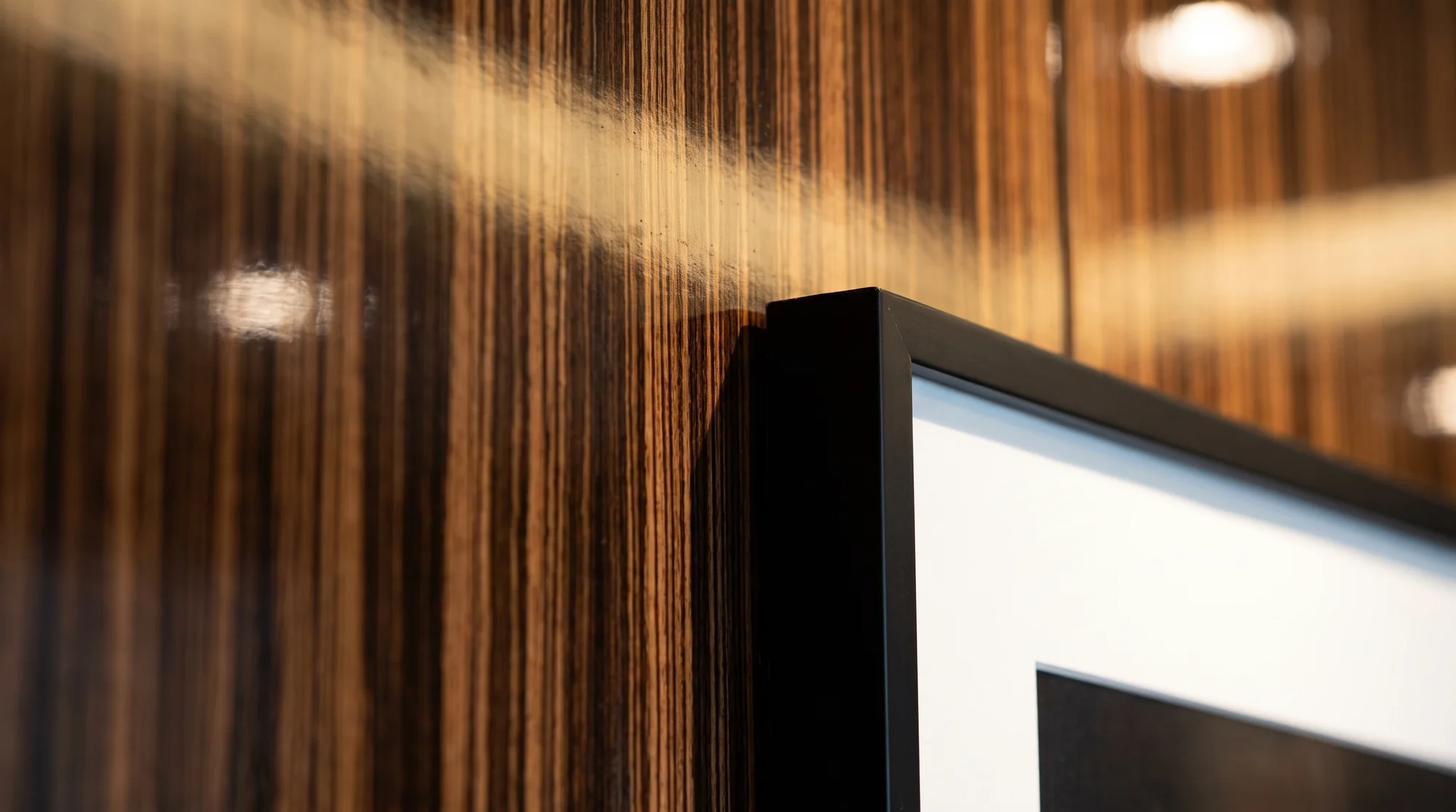Corner of a black picture frame on high-gloss macassar ebony panelling