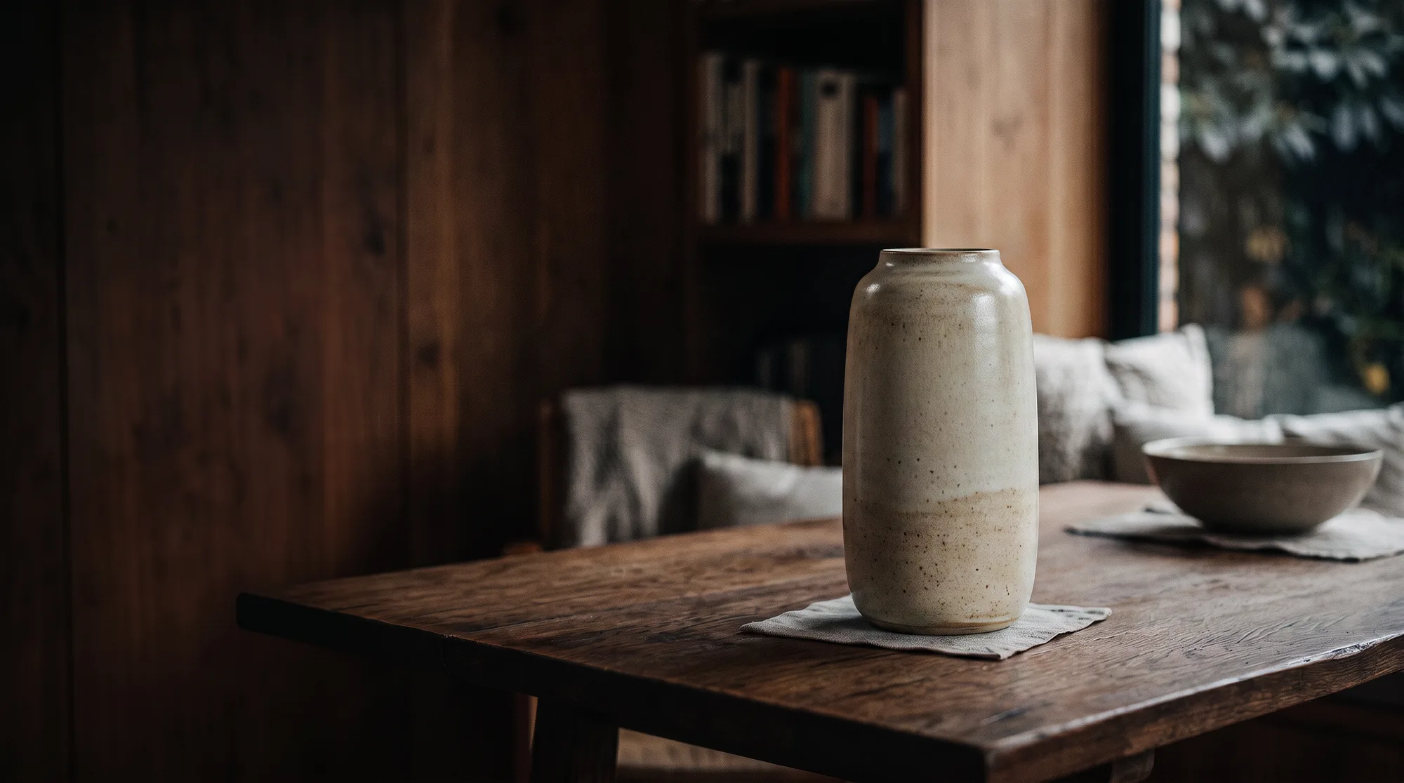 A cream ceramic vase on a wooden table in a warm interior