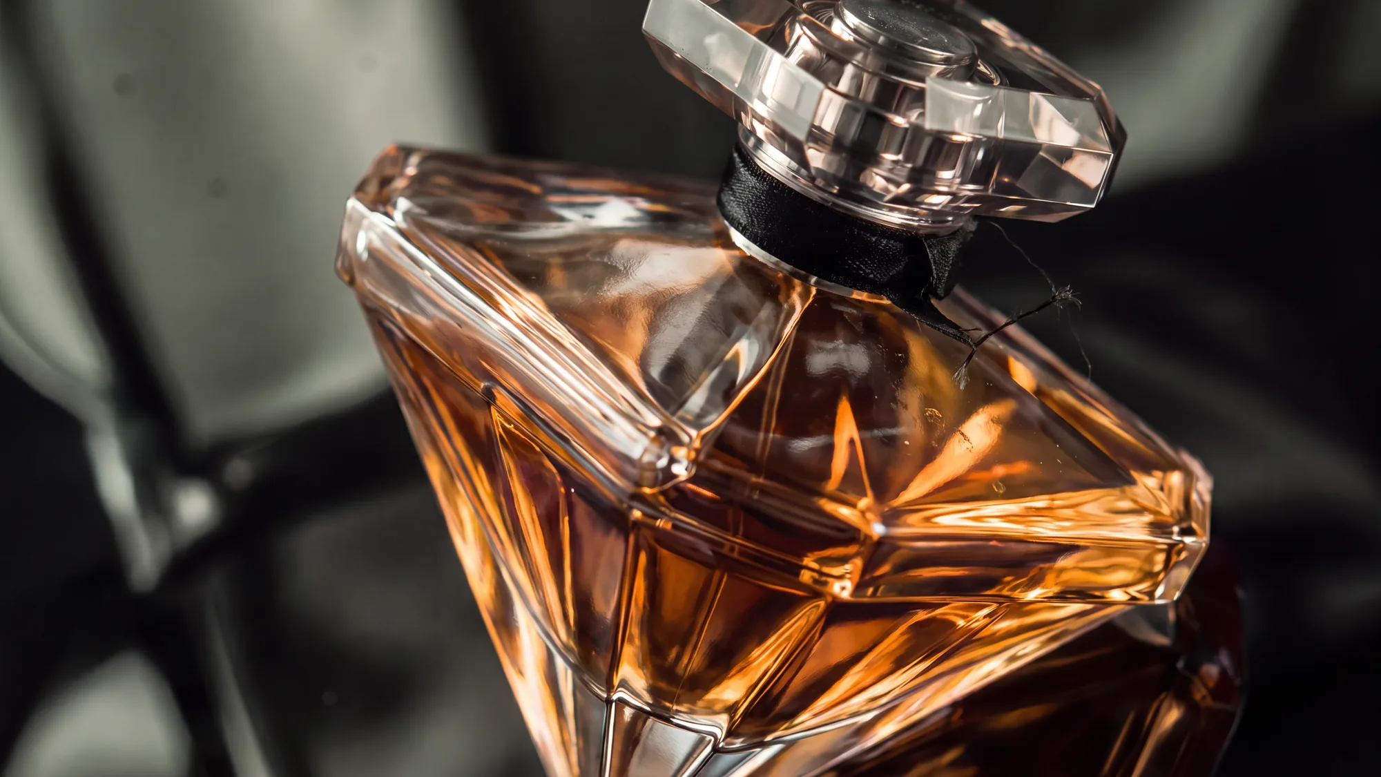 A macro shot of a perfume bottle's neck and stopper, with a loose thread and dust caught on the glass
