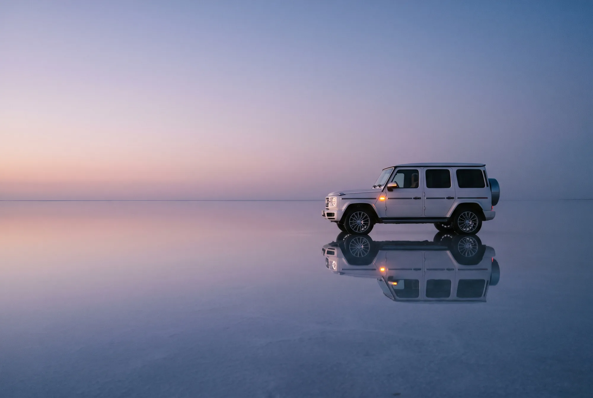 A white Mercedes-Benz G-Class on a mirror-smooth salt flat at dusk
