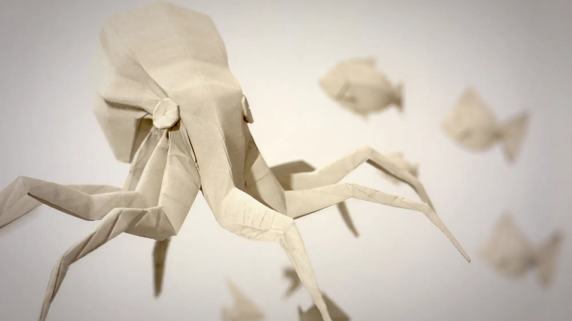 Origami octopus close-up — paper figure with outstretched tentacles, paper fish blurred in background