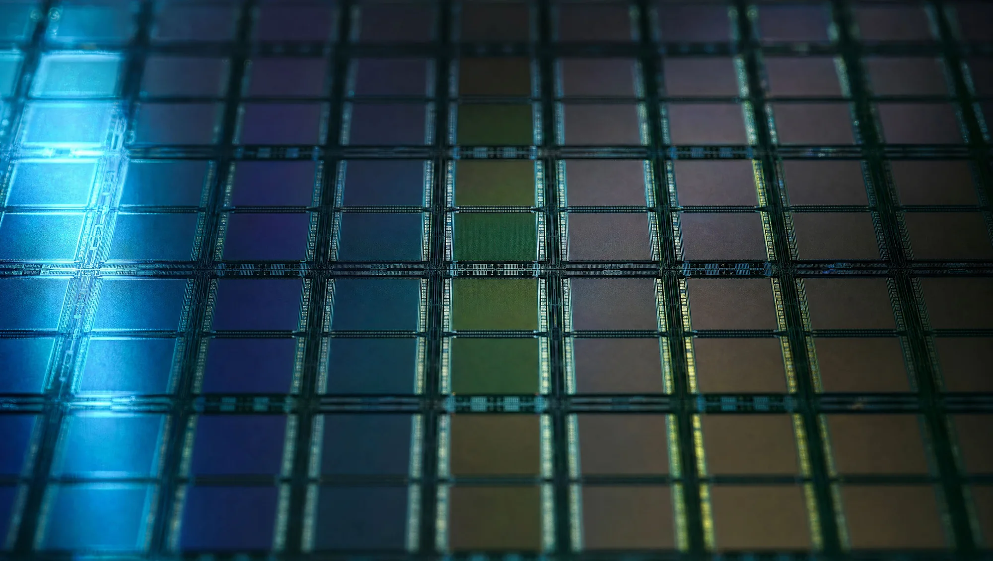 Extreme close-up of a wafer surface, a grid of chip dies in shifting blue, green and amber hues