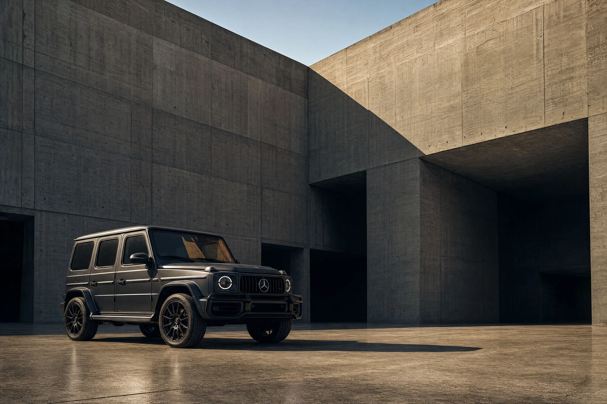 Dark grey G-Class three-quarter front view beside a concrete building in daylight