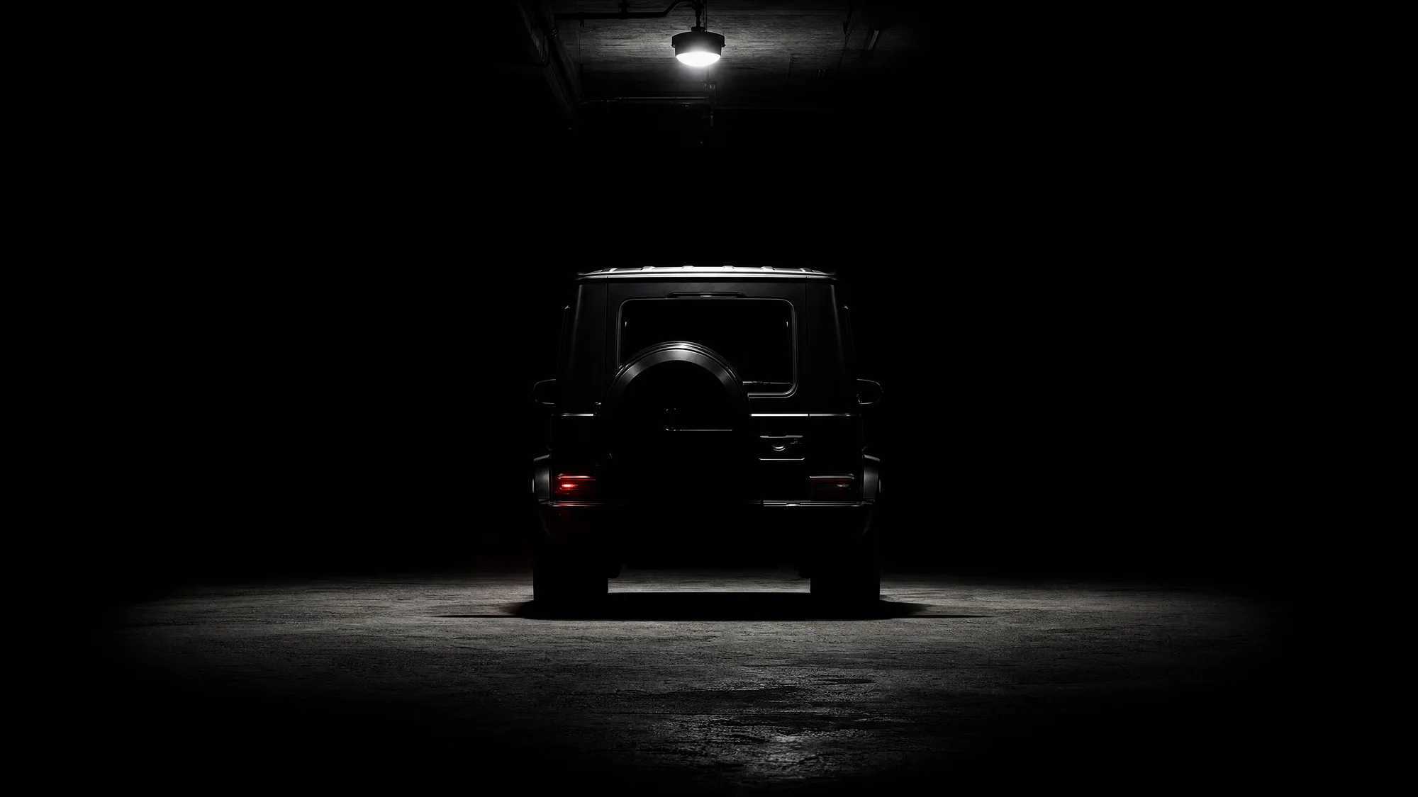 Black G-Class rear view in a dark studio, lit only by a single overhead lamp