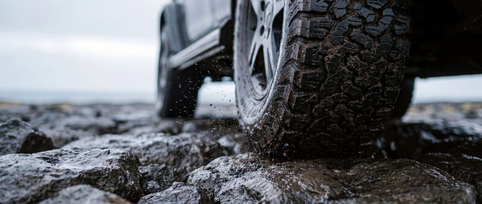 Close-up of a G-Class wheel on wet rocks, mud splashing from the tyre